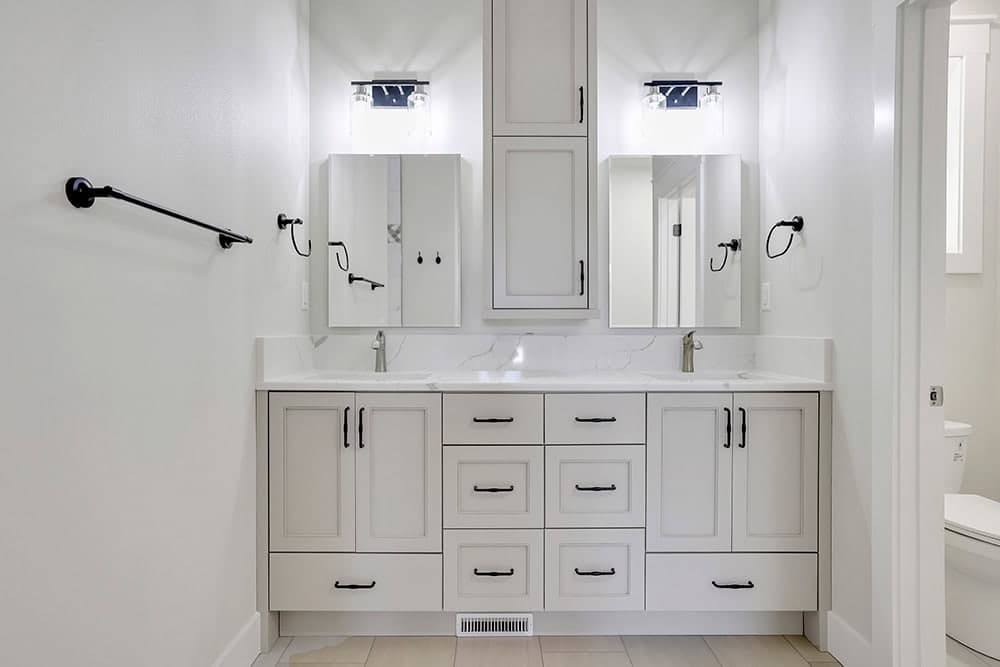 A double-sink bathroom vanity with painted shaker-style cabinets and a tall center cabinet