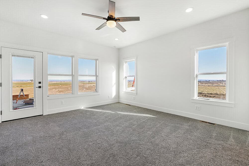 A bright room with several large windows and a glass door looking out over open ground